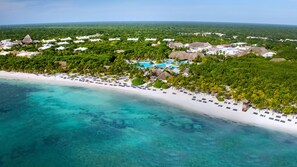 Vue aérienne d’un complexe hôtelier avec une plage, des eaux turquoise cristallines et une végétation luxuriante.