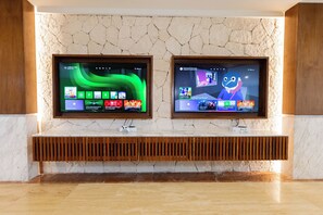 Two large flat-screen TVs mounted on a wall with a wooden console below. - Family Selection At Grand Palladium Kantenah (Kantenah)