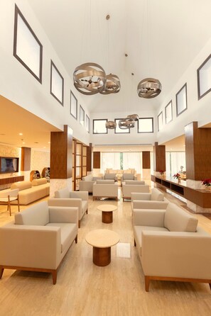 A spacious lobby with multiple seating areas, a central coffee table, and a television mounted on the wall. - Family Selection At Grand Palladium Kantenah (Kantenah)