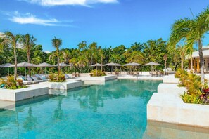 Un área de piscina con sillones y sombrillas, rodeada de palmeras y vegetación.