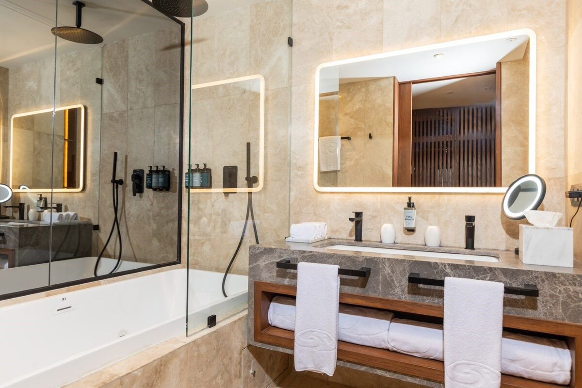 Une salle de bain moderne avec une douche en verre, un grand miroir et un meuble-lavabo doté d’un plan de travail en marbre.