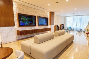 A modern living room with a beige sofa, a stone wall, two large flat-screen TVs, and a wooden entertainment unit. - Family Selection At Grand Palladium Kantenah (Kantenah)