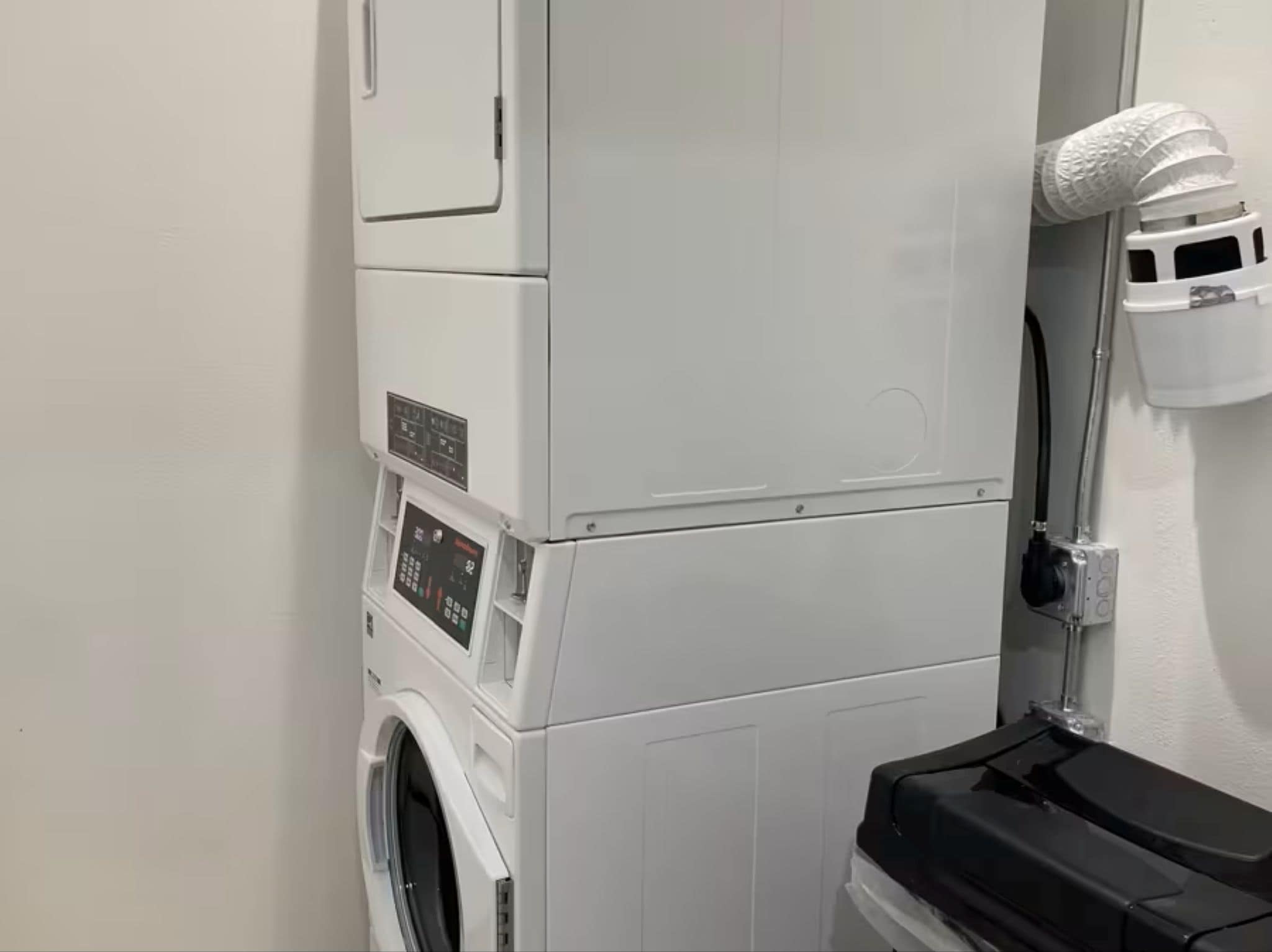 A compact laundry facility with stacked washing machines and dryers, a control panel, and a hose for water connection.