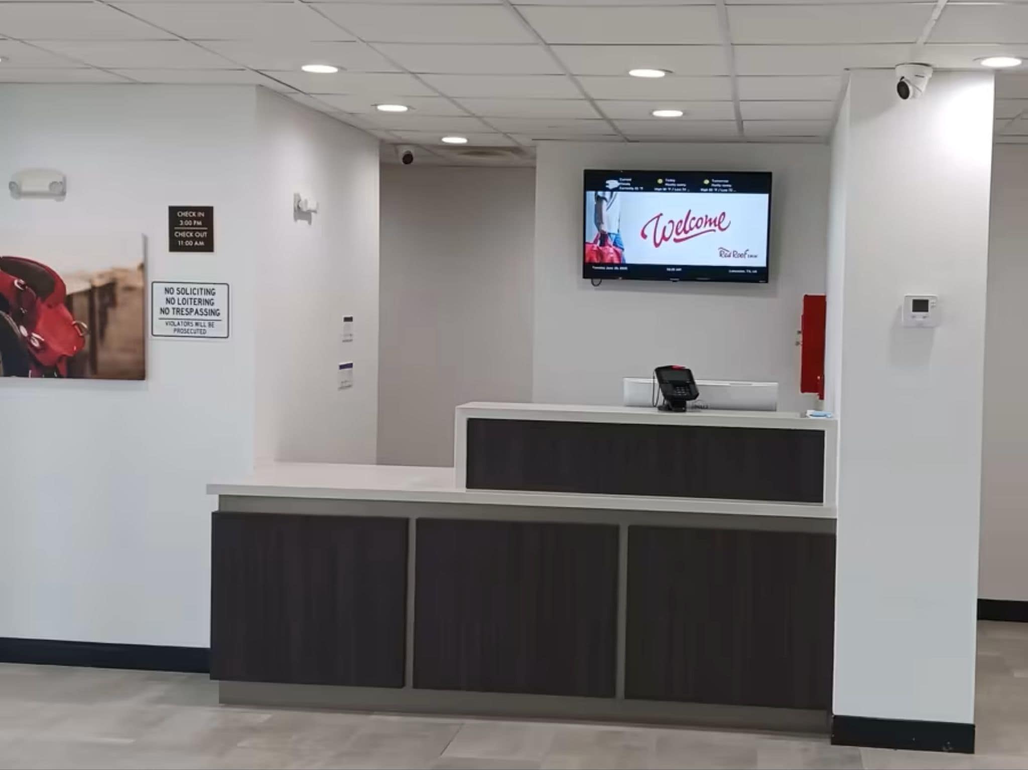A reception area with a digital screen displaying "Welcome" and a sign indicating check-in and check-out times.