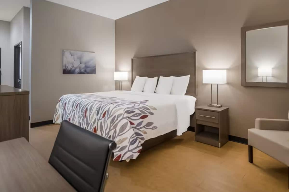 Quarto de hotel com uma cama grande, duas mesas de cabeceira com luminárias, uma escrivaninha, uma cadeira e um espelho na parede.