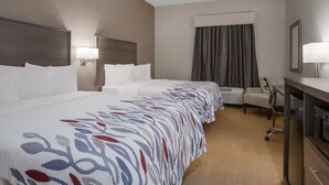Ein Hotelzimmer mit einem langes Bett, einem Schreibtisch, einem Sessel und einer Klimaanlage.