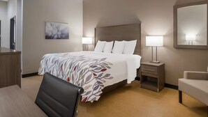 Ein Hotelzimmer mit einem großen Bett, zwei Nachttischen mit Lampen, einem Schreibtisch, einem Sessel und einem Spiegel an der Wand.