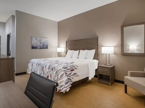 Une chambre d’hôtel avec un grand lit, deux tables de chevet avec des lampes, un bureau, une chaise et un miroir au mur.