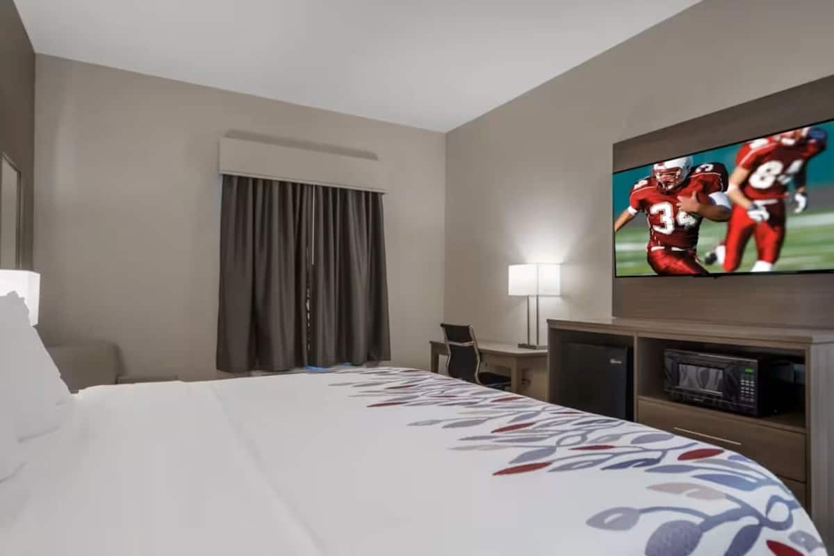 Quarto de hotel com cama, escrivaninha, televisão e janela com cortinas.