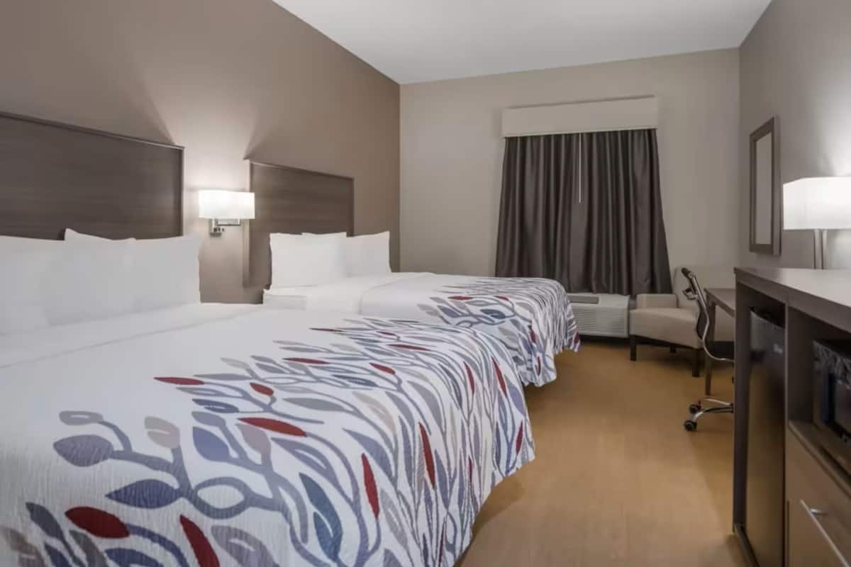 Quarto de hotel com uma cama grande, uma escrivaninha, uma cadeira e um ar condicionado.