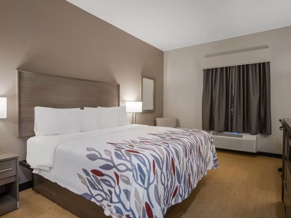 Une chambre d’hôtel avec un grand lit, une table de chevet, une lampe, une fenêtre avec des rideaux et un climatiseur fixé au mur.