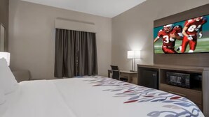 Ein Hotelzimmer mit einem Bett, einem Schreibtisch, einem Fernseher und einem Fenster mit Vorhängen.
