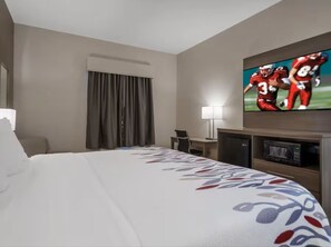 Une chambre d’hôtel avec un lit, un bureau, une télévision et une fenêtre avec des rideaux.