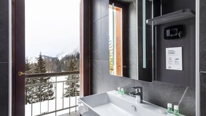 A modern bathroom with a large sink, a mirror, and a view of snowy mountains through a balcony door.