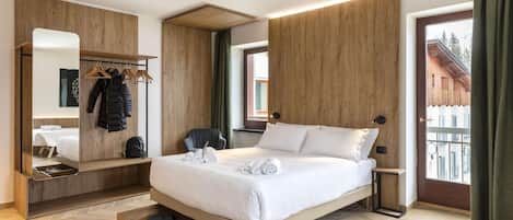 Una habitación de hotel moderna con estructura de cama de madera, armario empotrado, zona de estar y vistas al exterior.