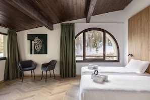 Una habitación con dos camas, techo de madera, un gran ventanal de arco con vista nevada y una obra de arte geométrica en la pared.