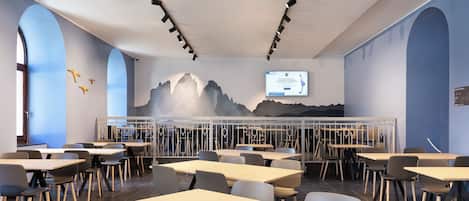 Un espace de restauration moderne, avec des tables et des chaises, une fresque murale et un écran de télévision diffusant une publicité.