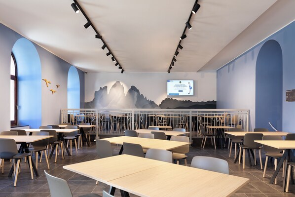 Un comedor moderno con mesas y sillas, un mural en la pared y una pantalla de televisión mostrando un anuncio.