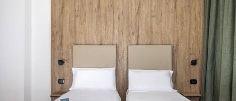 A double bed with two pillows and a folded towel, a wooden headboard, and a nightstand with a phone.