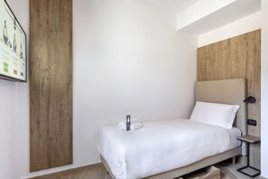 Habitación de hotel con cama, pared decorativa de madera, mesita de noche pequeña y televisor instalado en la pared.