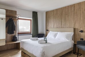 A hotel room with a bed, a chair, a coat rack, and a window with curtains. - B&B Hotel Passo Tre Croci Cortina (Cortina d'Ampezzo)