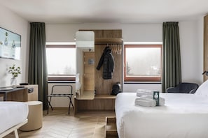 Habitación de hotel con una cama, un escritorio con una computadora portátil, una silla, un perchero y vistas a árboles a través de las ventanas.