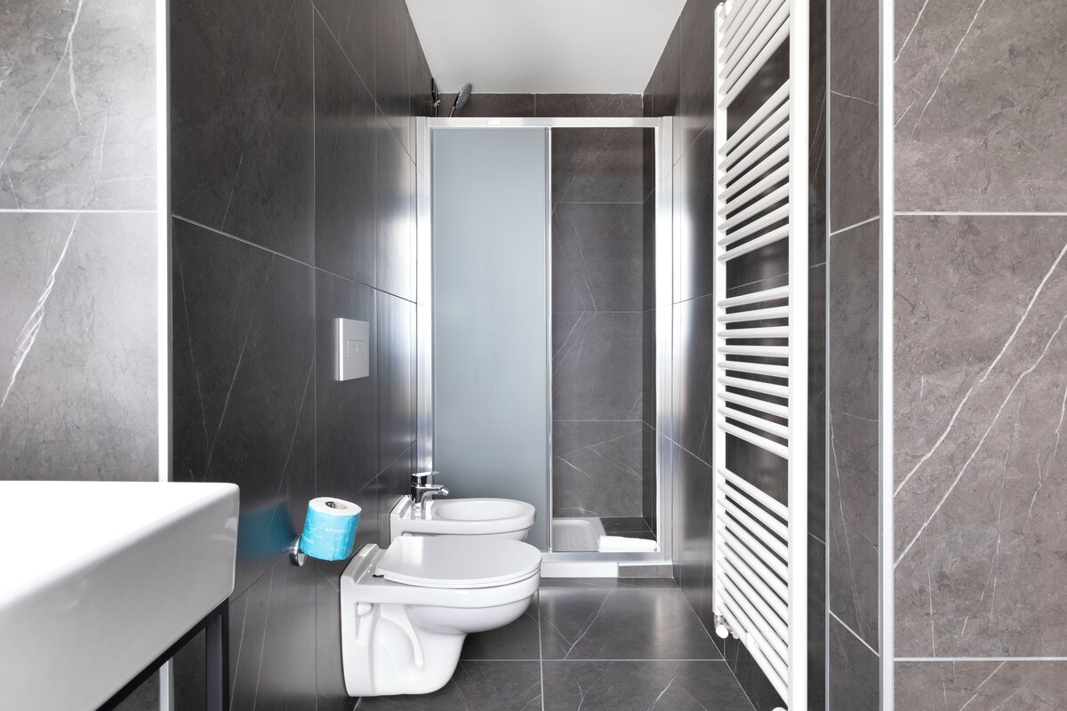 A modern bathroom with dark tiles, a shower, a toilet, and a bidet.