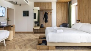 Una habitación de hotel moderna con una cama grande, un escritorio con una computadora portátil, una silla, un armario y un espejo.