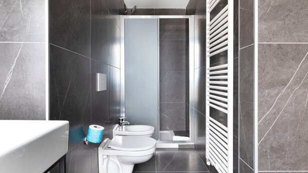 A modern bathroom with dark tiles, a shower, a toilet, and a bidet. - B&B Hotel Passo Tre Croci Cortina (Cortina d'Ampezzo)