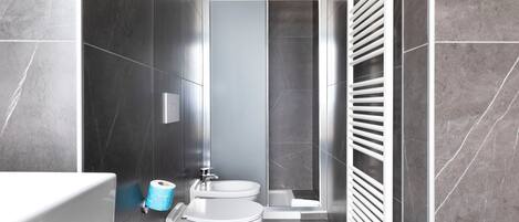 A modern bathroom with dark tiles, a shower, a toilet, and a bidet.