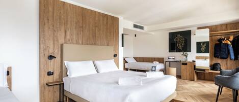 Habitación de hotel moderna con una cama grande, un panel de madera decorativo, un escritorio con silla, un armario y un zapatero.