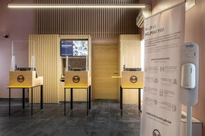 A hotel reception area with a wooden reception desk, a digital menu board, and a poster with COVID-19 guidelines. - B&B Hotel Passo Tre Croci Cortina (Cortina d'Ampezzo)