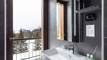 Casa de banho moderna com um espelho grande, uma sanita branca e vista para uma paisagem montanhosa coberta de neve através de uma porta varanda.