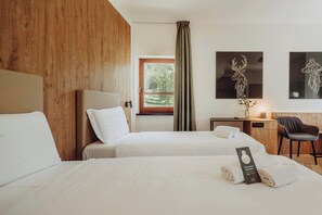 A hotel room with two beds, a desk, a chair, and artwork on the walls. - B&B Hotel Passo Tre Croci Cortina (Cortina d'Ampezzo)