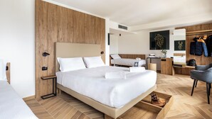 A modern hotel room with a large bed, a wooden accent wall, a desk with a chair, a wardrobe, and a shoe storage box.