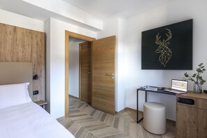A modern hotel room with a bed, a desk with a laptop, a small stool, and a wall-mounted artwork. - B&B Hotel Passo Tre Croci Cortina (Cortina d'Ampezzo)