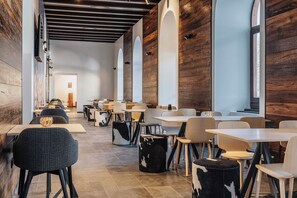 Un interior de restaurante moderno con paredes de madera, varias mesas y sillas, y una larga barra.
