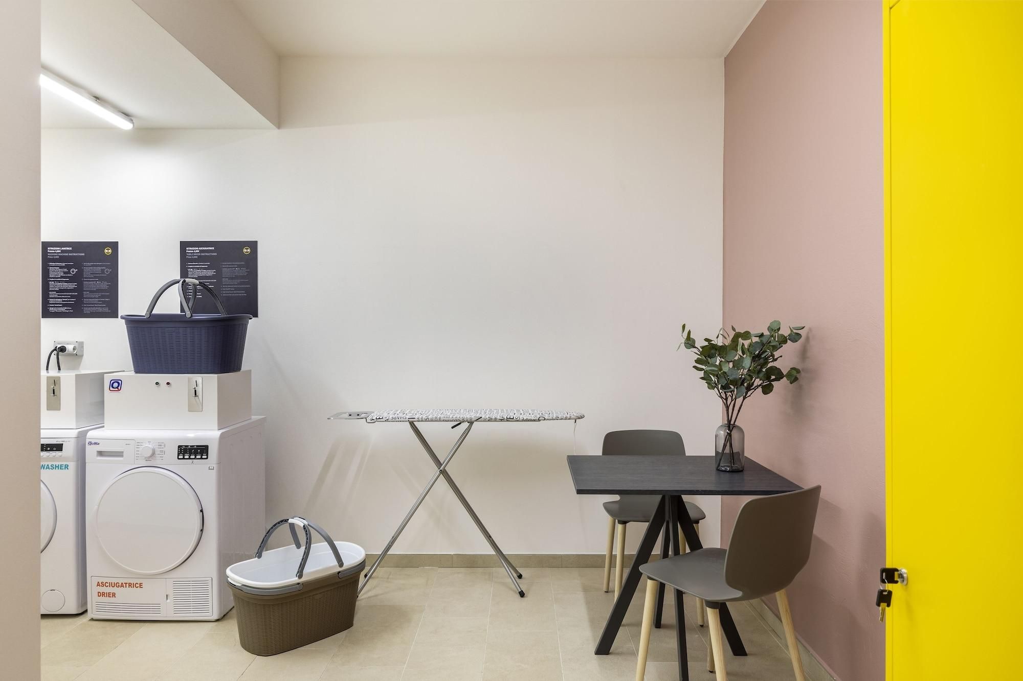 Ein kleines Zimmer mit Waschmaschine, Trockner, Tisch und Stühlen sowie einer kleinen Pflanze.
