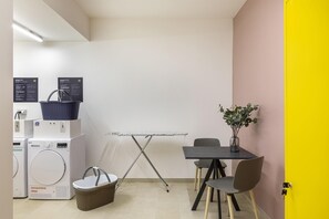 A compact room with a washing machine, a dryer, a table with chairs, and a small plant. - B&B Hotel Passo Tre Croci Cortina (Cortina d'Ampezzo)