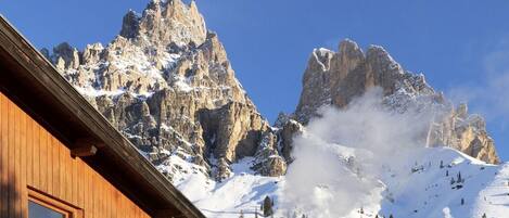 A wooden building with multiple windows and balconies, set against a backdrop of snow-covered mountains and clear blue sky.