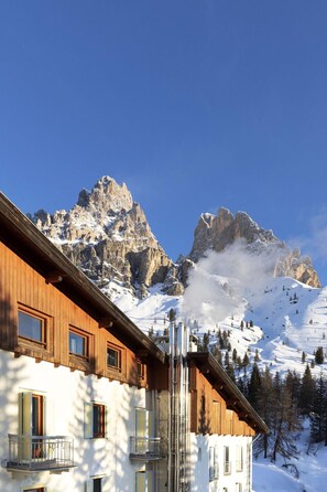 A wooden building with multiple windows and balconies, set against a backdrop of snow-covered mountains and clear blue sky. - B&B Hotel Passo Tre Croci Cortina (Cortina d'Ampezzo)