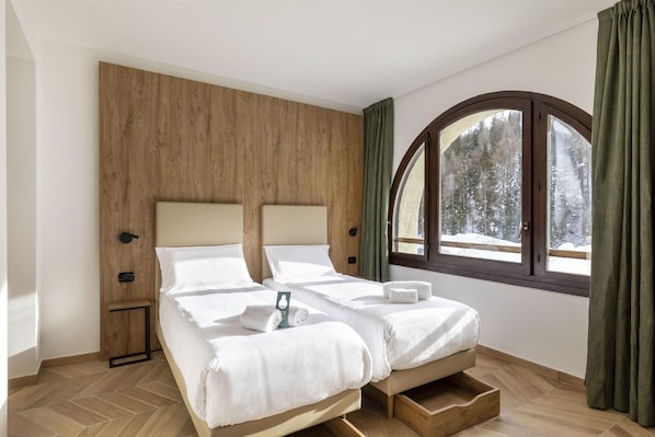 A double bed with a wooden headboard, a bedside table, a window with a view of trees, and a green curtain. - B&B Hotel Passo Tre Croci Cortina (Cortina d'Ampezzo)