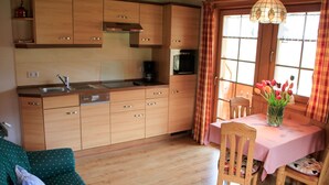 A wooden kitchen with a dining table and chairs, a sofa, and a window with curtains. - Apartment 'Feldberg' with Shared Garden, Balcony and Wi-Fi (Hinterzarten)