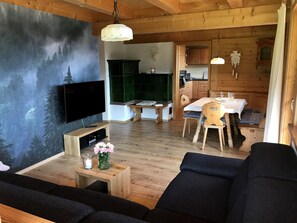 A cozy living room with a flat-screen TV, wooden furniture, a dining area with a table and chairs, and a kitchen visible in the background. - Holiday Apartment 'Hirschsprung' with Mountain View, Private Terrace and Wi-Fi (Hinterzarten)