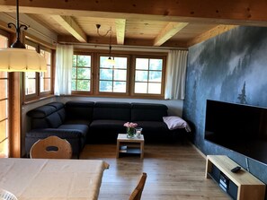 A cozy living room with a sectional sofa, a TV, and a wooden floor. - Holiday Apartment 'Hirschsprung' with Mountain View, Private Terrace and Wi-Fi (Hinterzarten)