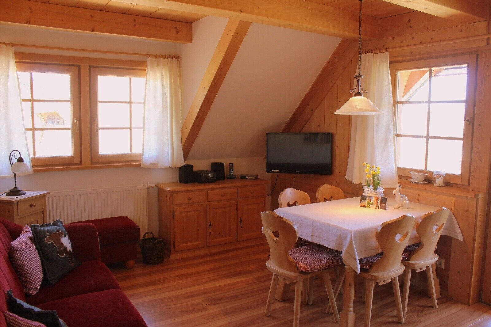 Ein gemütliches Zimmer mit Esstisch, Stühlen, Fernseher und einem roten Sofa.
