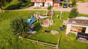 Un espace de jeux extérieur clôturé, équipé d’un toboggan, de balançoires et d’un bac à sable.