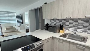 Una cocina moderna con estufa, horno y lavaplatos integrados, armarios de madera clara y salpicadero de azulejos.