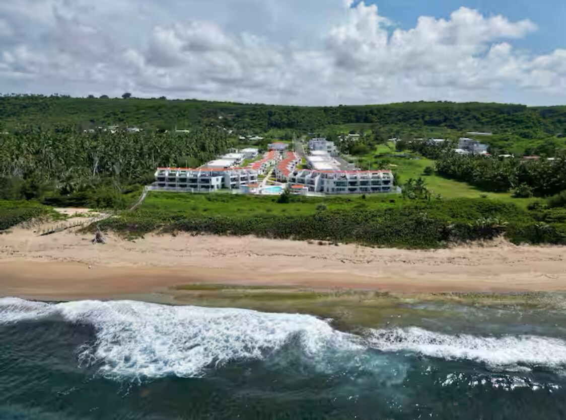 Um hotel à beira-mar com vários edifícios, uma praia e vegetação exuberante.