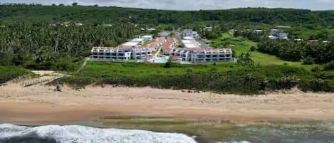 Um hotel à beira-mar com vários edifícios, uma praia e vegetação exuberante.